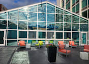 Thumbnail 39 of 40 - A glass building with orange chairs and a black planter in front.