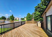 Thumbnail 11 of 22 - A wooden deck overlooks a body of water with a house and trees in the background.