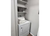 Thumbnail 9 of 22 - A white laundry machine is in a cabinet with towels on top.