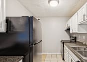 Thumbnail 5 of 17 - A kitchen with a black refrigerator and white cabinets.