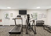 Thumbnail 12 of 17 - A gym with a treadmill, a stationary bike, and a bench press.