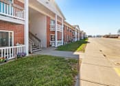 Thumbnail 4 of 14 - A row of red brick apartment buildings with white railings and steps leading to the doors.