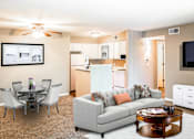 Thumbnail 9 of 35 - A living room with a grey couch, a coffee table, and a dining table with chairs.