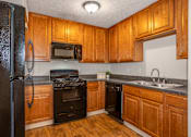 Thumbnail 19 of 23 - A kitchen with wooden cabinets and black appliances.