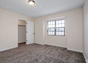 Thumbnail 33 of 35 - A room with a carpeted floor, a window with blinds, and a door.