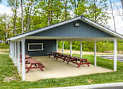 Thumbnail 42 of 57 - A pavilion with picnic tables is surrounded by trees.