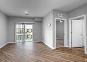 Thumbnail 53 of 57 - A room with a sliding glass door leading to a balcony, hardwood floors, and white walls.