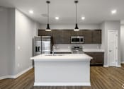 Thumbnail 39 of 57 - A modern kitchen with a white island and dark brown cabinets.
