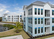 Thumbnail 46 of 49 - A modern two-story building with blue and white exterior and a black fence surrounding a grassy area.at Imperial Crossing Luxury Apartment Homes, Bonita Springs, FL