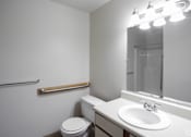 Thumbnail 5 of 26 - A white bathroom with a toilet, sink, mirror, and lights.
