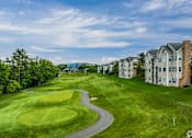 Thumbnail 26 of 27 - A golf course with a green and a building in the background.