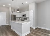 Thumbnail 51 of 53 - A kitchen with a white island and pendant lights.