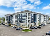 Thumbnail 6 of 53 - A large apartment complex with a parking lot in front.