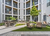 Thumbnail 14 of 53 - A patio area with chairs and tables is surrounded by apartment buildings.