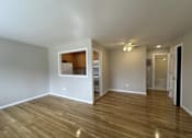 Thumbnail 4 of 9 - A room with wooden floors and a small kitchenette in the corner.