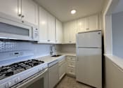 Thumbnail 5 of 9 - A white kitchen with a stove, microwave, and refrigerator.