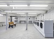 Thumbnail 12 of 13 - A laundromat with a row of washing machines and a bench.