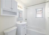 Thumbnail 11 of 13 - A white bathroom with a toilet, sink, and bathtub.