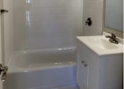 Thumbnail 7 of 9 - A white bathroom with a white tub and sink.