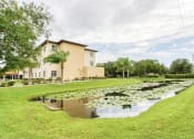 Thumbnail 12 of 12 - pond with lily pads, lush grass, and mature trees beside Holy Cross Manor I