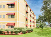 Thumbnail 3 of 24 - Casa San Pablo senior apartments exterior with mature trees and trim grass