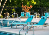 Thumbnail 4 of 26 - a pool with blue chaise lounge chairs and a poolside table