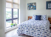 Thumbnail 73 of 82 - 1-BR Apartments in Beverly, MA - Holmes Beverly - Furnished Bedroom with Wood Flooring, a Bed, Framed Art, White Walls, LArge Window with Blinds, and Attached Nightstands