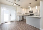 Thumbnail 3 of 17 - View of open kitchen with wood look flooring, stone counters, white cabinets, stainless appliances, ceiling fan, and lighting