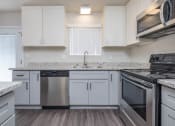 Thumbnail 4 of 17 - Closer look at kitchen with stone counters, white cabinets, stainless appliances, white cabinets, and window above sink