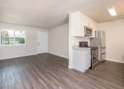 Thumbnail 7 of 17 - View of living and kitchen area with wood look flooring, well lit window in living area, stone counters in kitchen, stainless appliances, and white cabinets.