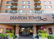 Thumbnail 1 of 25 - The Dunton Tower building has a red brick facade and a sign above the entrance.
