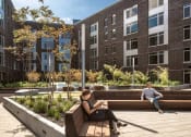 Thumbnail 9 of 36 - Person sitting reading on bench in sunlit courtyard