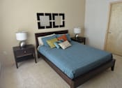 Thumbnail 6 of 26 - A bed with a blue comforter and a lamp on a side table.