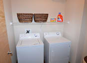 Thumbnail 3 of 26 - A laundry room with a washing machine, a dryer, and a shelf above them.