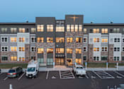 Thumbnail 11 of 11 - an exterior view of an apartment building at dusk with cars parked in front