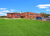 Thumbnail 27 of 31 - The brick exterior, parking lot, and large green space at Muskego School Apartments
