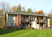 Thumbnail 6 of 27 - A large brick building with a balcony and a green lawn in front.