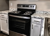 Thumbnail 20 of 27 - A modern kitchen with a black stove top oven and white cabinets.