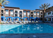 Thumbnail 7 of 33 - A swimming pool surrounded by lounge chairs and umbrellas in front of apartment buildings.