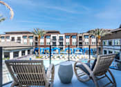 Thumbnail 5 of 33 - A balcony with two chairs and a table overlooking a pool.