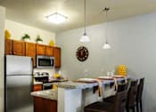Thumbnail 2 of 22 - Liberty Gateway Apartments, Salt Lake City, Utah, kitchen with bar seating, refrigerator, microwave, oven, and a clock on the wall.