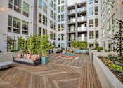 Thumbnail 2 of 73 - A wooden deck with a bench and plants in the foreground and apartment buildings in the background.