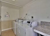 Thumbnail 22 of 22 - a laundry room with three washing machines and a counter with a sink