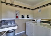 Thumbnail 6 of 22 - A white washing machine sits in a small room with a trash can and a fire extinguisher on the wall.