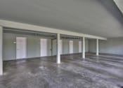 Thumbnail 11 of 42 - A large empty room with concrete floors and white pillars.