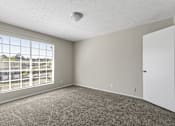 Thumbnail 6 of 47 - A room with a carpeted floor, a window with blinds, and a white door.