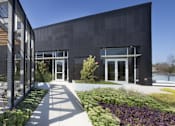 Thumbnail 5 of 16 - A modern building with a black facade and a garden in front.