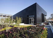 Thumbnail 6 of 16 - A modern black building with a garden in front.