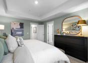 Thumbnail 19 of 33 - A bedroom with a large bed and a dresser with a lamp on top.
