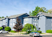 Thumbnail 6 of 7 - a blue apartment building with cars parked in front of it